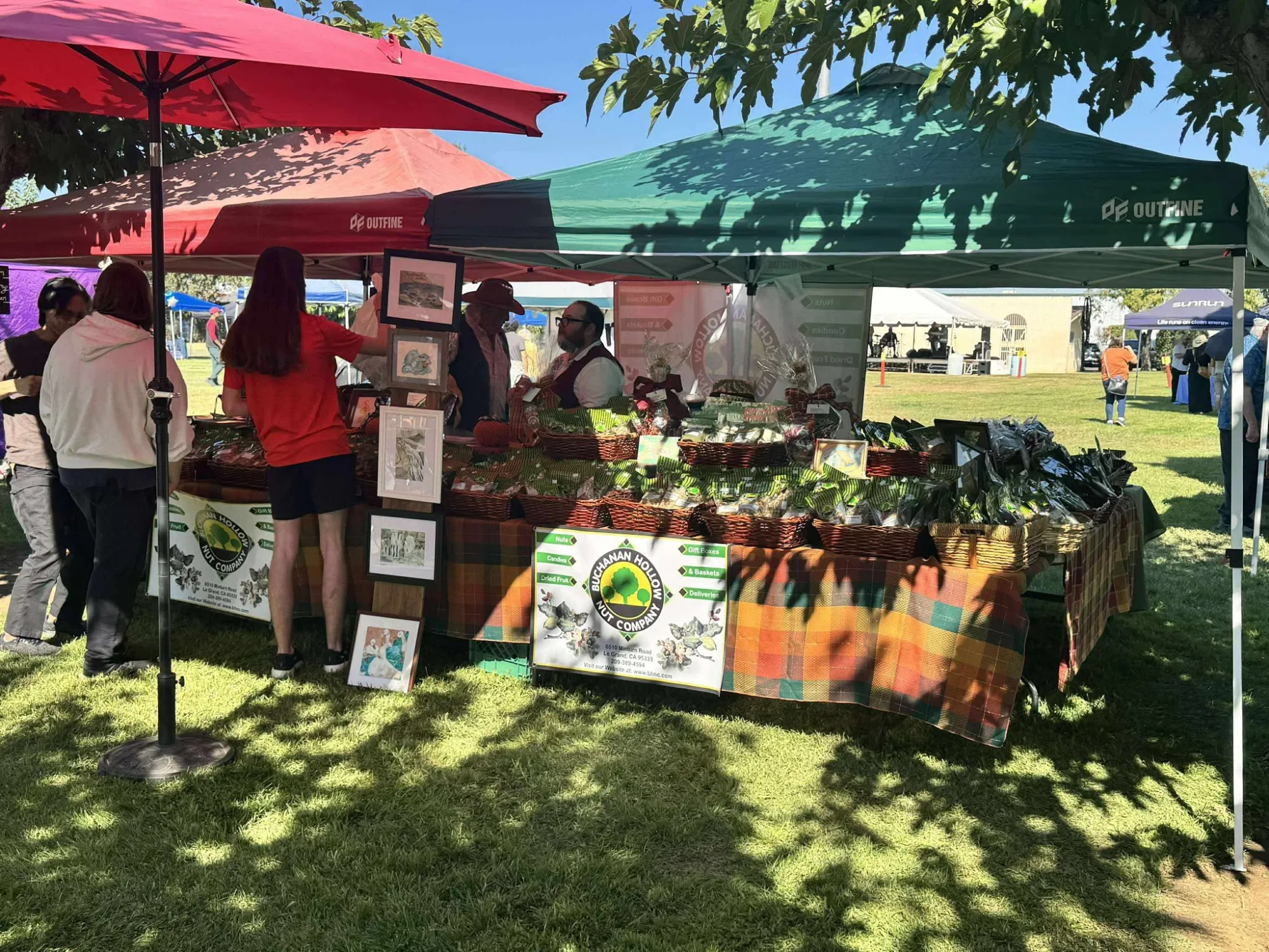 The Buchanan Hollow Nut Company booth setup at an outdoor Merced community market on a bright, sunny day.