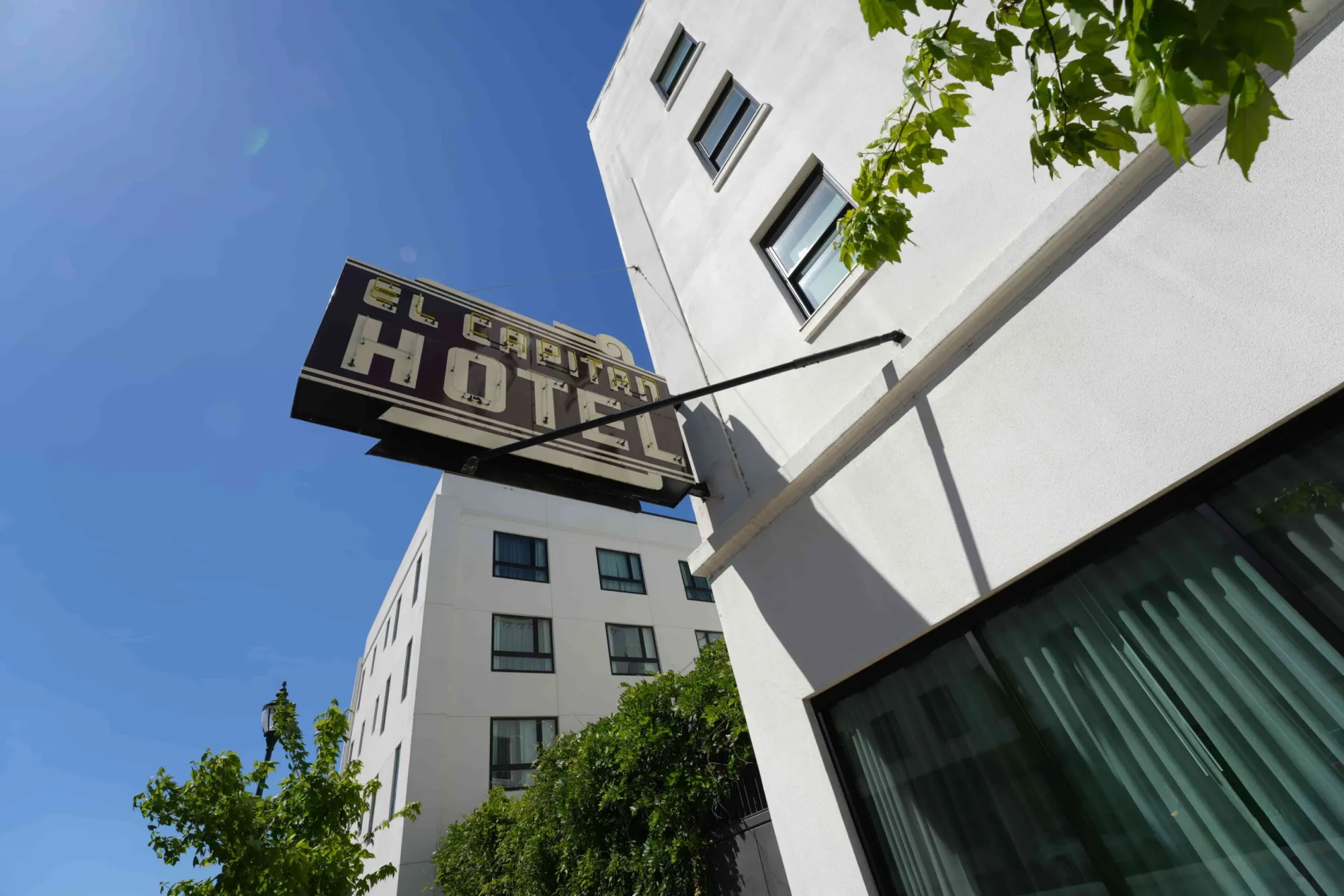 Looking up at the classic dark brown and white El Capitan Hotel sign on a modern white multistory building facade.