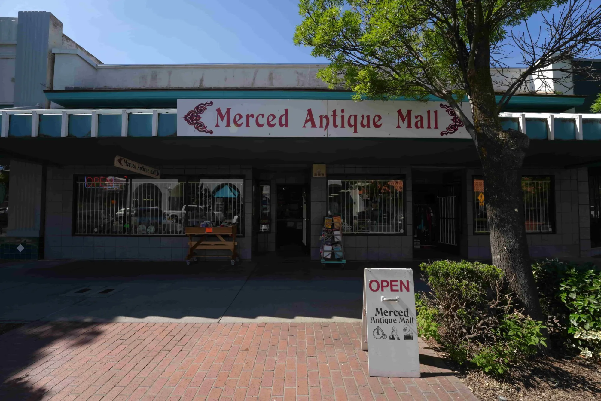 The exterior storefront of the Merced Antique Mall with an open sign displayed on the brick sidewalk.