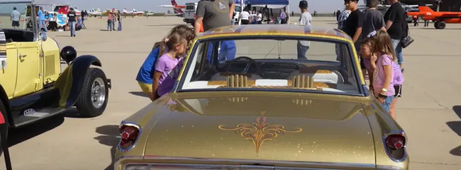 Visitors admiring custom classic vehicles and lowriders at a Merced community car show and aviation tarmac event.