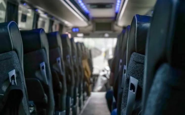 Interior view looking down the aisle of an empty modern charter bus with dark plush seating and blue overhead lighting.