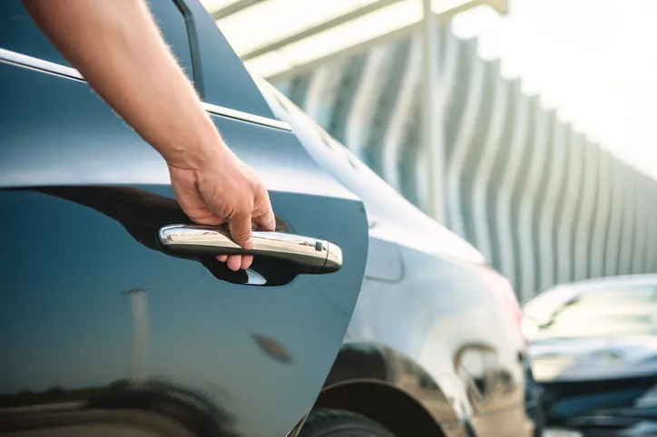 Close-up of a person's hand opening the door of a black luxury sedan.
