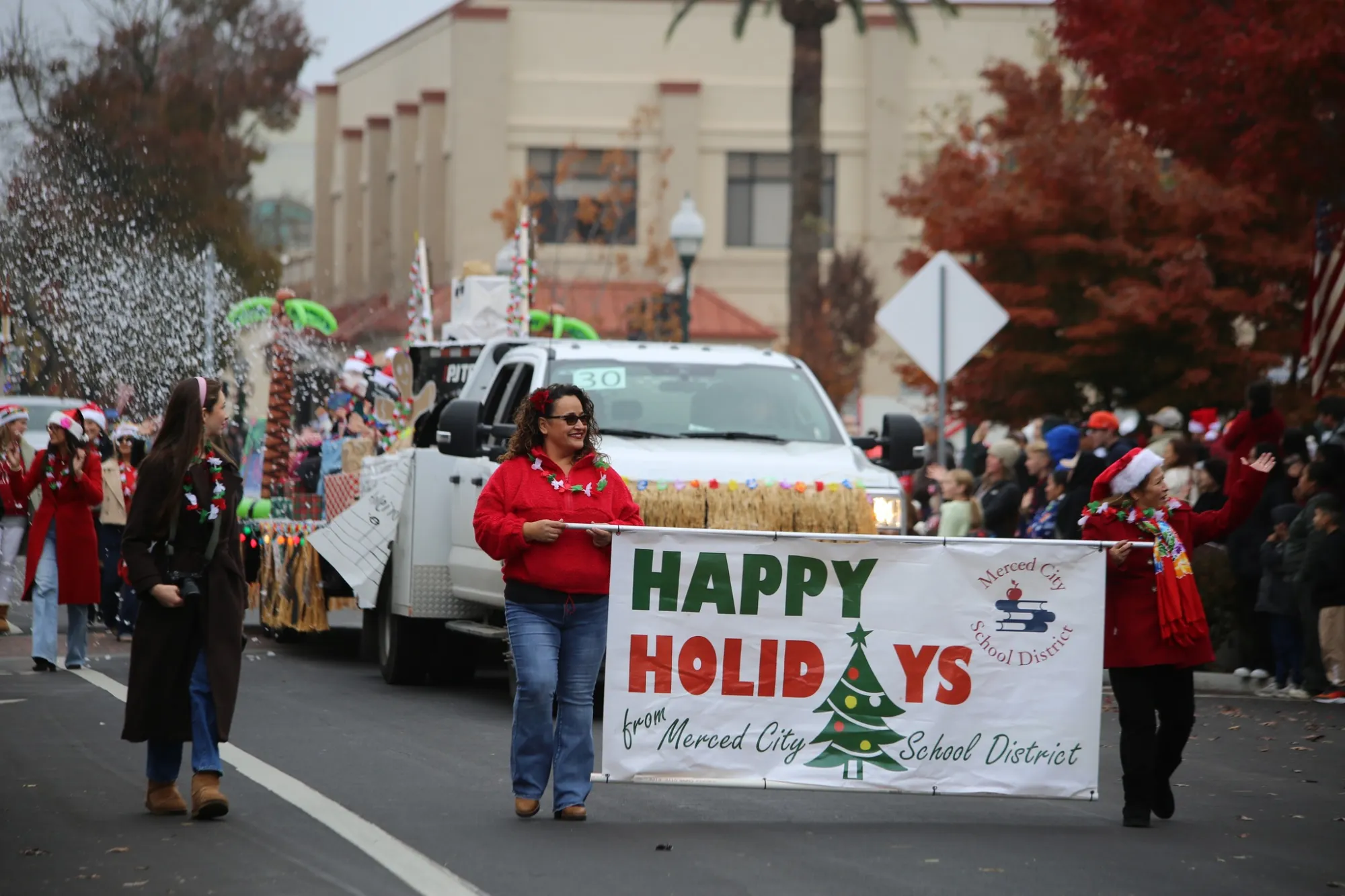 Marchers carry a "Happy Holidays" banner from Merced City School District along a parade route