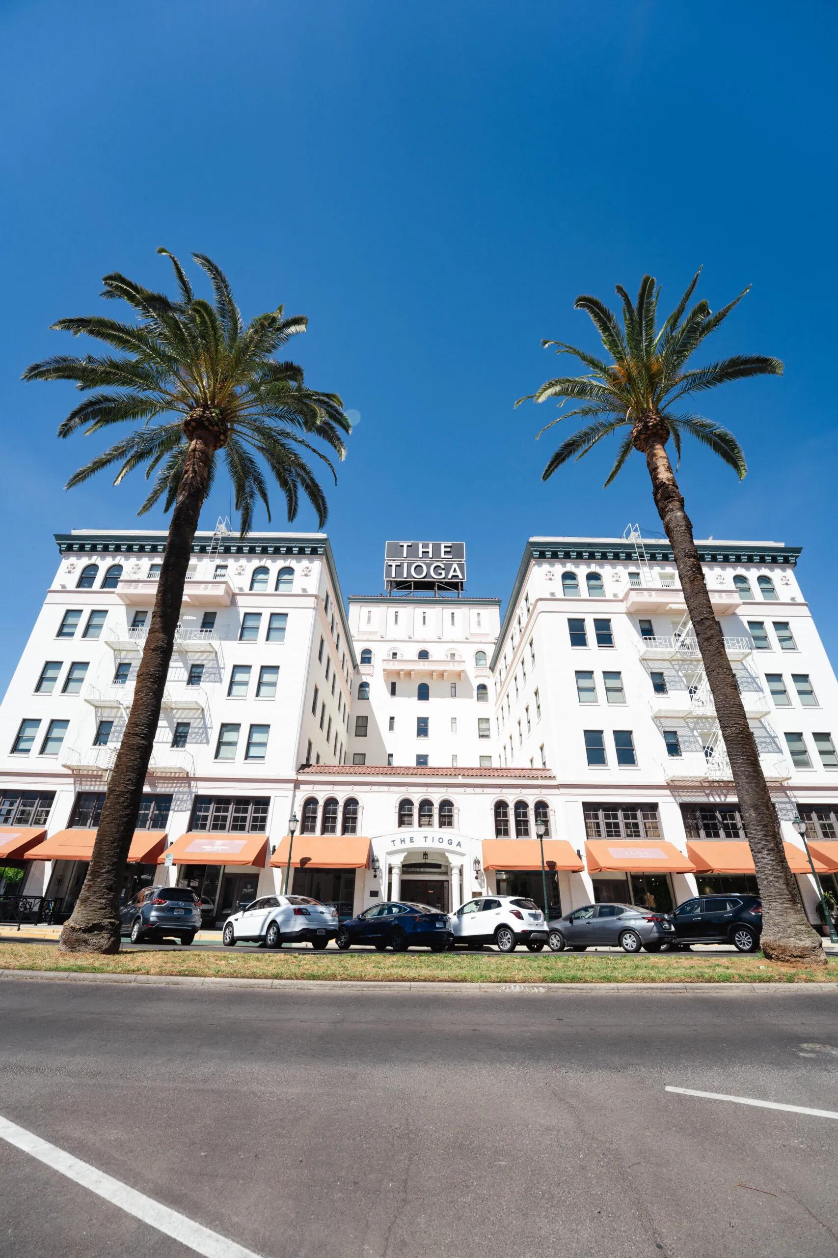 Two tall palms framing the Tioga building's white facade and orange awnings