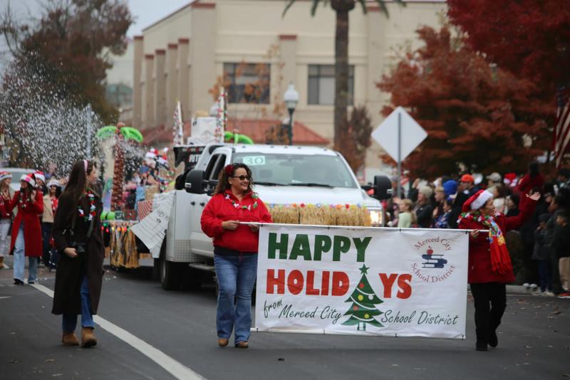 Marchers carry a "Happy Holidays" banner from Merced City School District along a parade route
