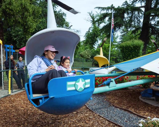 A mother and young daughter smiling together on Kiddieland’s blue helicopter ride