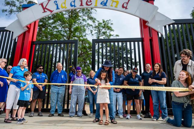 A child cutting the ribbon at the Kiddieland entrance surrounded by community members